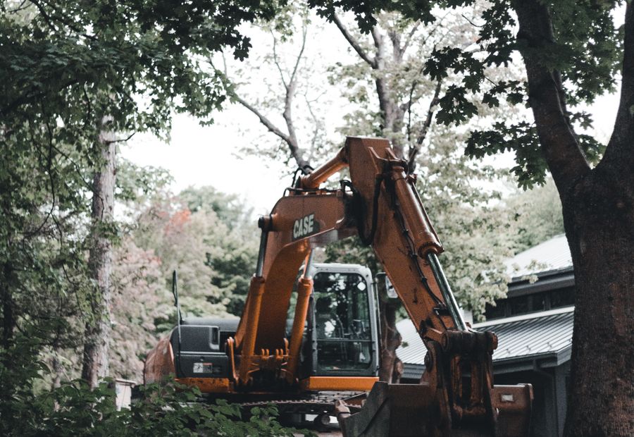 Excavator working beside a house surrounded by trees on a Duluth septic job